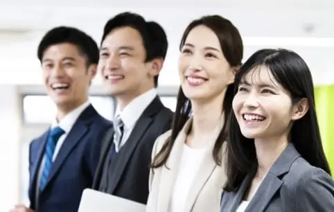 スーツ姿の男性二人と女性二人が横並びで笑顔を浮かべている